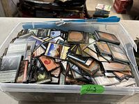 Top view of clear plastic bin filled with assorted Magic The Gathering cards facing up and down, showing various card art and backs.