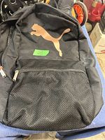 Front of black Puma backpack showing gold Puma logo and front mesh zippered pocket