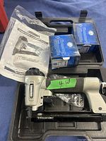 Surebonder air stapler in black carrying case with two blue boxes of staples and instruction manual visible.