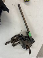 Photo of vintage come-a-long with long handle and attached heavy chain on white surface