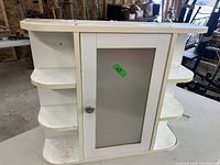 Front view of white wall cabinet with a single door featuring a translucent textured panel and knob and open shelving on each side.