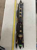 Full view of the carved wooden wall hanging mask on a white surface showing detailed carving and painted accents.