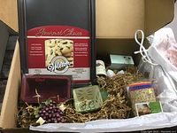 Box contents showing Wilton baking pan, silicone loaf molds, apron, muffin cups, and other baking accessories all set in straw packing material.