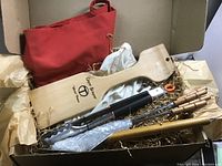 Photo showing BBQ set laid inside box including wooden spatula, tongs wrapped in bubble wrap, wooden scraper, skewers, and red apron.