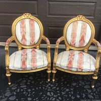 Front view of the two armchairs showing the rounded backs and striped upholstery with gilded carved wooden frames.