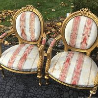 Pair of vintage style gilded armchairs with vertical striped upholstery and carved floral medallion tops.