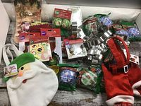 Photo showing various metal cookie cutters, multiple packs of holiday-themed baking cups, and two fabric gift bags with Santa themes