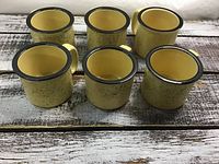 Six yellow heavy weight coffee mugs with black rims on rustic wood surface