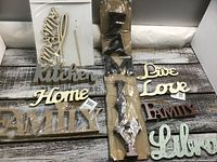 Photo showing multiple wooden crafting words including 'Love', 'Live', 'Kitchen', 'Home', 'Family', and 'Life'. 'Family' is broken and partially missing pieces. Words come in different colors such as gold, white, brown, and silver.
