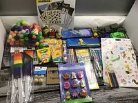 Overall view of the kids crafting items on a surface including pom-poms, stickers, pencils, markers, pencil cases, toy cars and more.