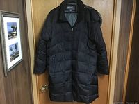Full front view of the black Eddie Bauer winter coat with front zipper and two zippered pockets, hanging on a door.