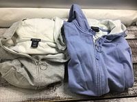 Two folded Gap hoodies, one grey and one blue, showing the attached hoods and zipper pulls.