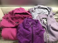 Three ladies hoodies folded and overlapping, showing the colors and partial logos.
