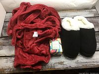 Red polyester housecoat next to black fleece-lined slippers and a small decorative box on wooden floor