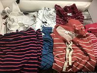 Pile of 7 assorted ladies sweaters in various colors and patterns, including coral, maroon, black/pink stripes, blue ribbed, white with spots, maroon and pink sweaters.