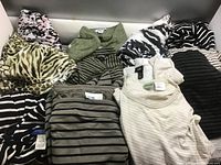 Photo showing various ladies sweaters and activewear tops laid out showcasing different patterns and colors including zebra print, leopard print, stripes, and solids.