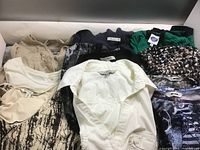 Nine assorted ladies tops and blouses laid out, including cream, white, black, and patterned fabrics.