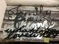 Photo of six metal word signs stacked together on wooden surface showing different styles and colors.