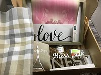 Overall lot content with table runner, framed love sign, candle, pillow, wooden sign, and decorative sheet.