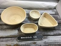 Four proofing dough baskets of various shapes and sizes shown on wooden surface: large round with coil pattern, small cloth-lined round, small oval coil, and triangular basket.