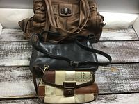 Three purses arranged on wooden surface: large brown handbag at back, mid-sized black crossbody purse in middle, and small patchwork clutch in front.