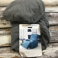 Grey textured slipcover folded with label showing recliner covered in blue slipcover to illustrate use.