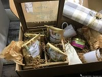 Photo of wooden box with loose leaf tea packages, cups, honey jar, creamer, cloth pouch, and napkin.