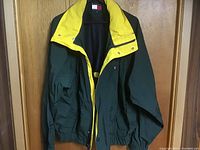 Tommy Hilfiger jacket hanging on a wooden door showing full front with dark green body and yellow inner collar.