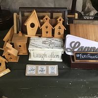 Photo showing various wood crafted items such as birdhouses, a painted box with text, wooden sign, and trays.