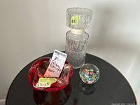 Photo shows MCM art glass ashtray, paperweight with floral design, and pressed glass decanter with stopper placed together on a dark surface.