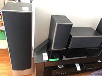 Photo showing two tall main floor-standing speakers and two smaller bookshelf rear speakers on a stand.