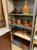 Photo showing four shelves of assorted woven baskets varying in size, shape and color, placed on a gray metal shelving unit against cement wall.