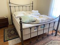 Full view of metal bed frame with mattress and box spring, bedding on top