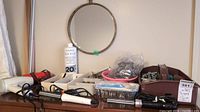 Wide shot showing the hanging mirror on the wall above a table with various hair tools and accessories arranged in trays and loosely.