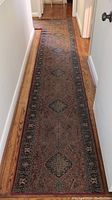 Full length view of the long section of the hallway runner on wood floor, showing its reddish base color and diamond floral motifs