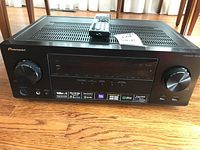 Front view of Pioneer VSX-824 AV receiver with remote on top, showing control knobs, display, and badges detailing features and supported streaming apps.