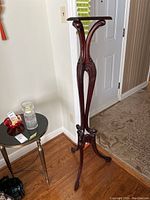 Full view of the tall wood veneer plant/display stand showing its curved legs and overall structure.