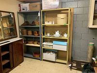 Photo showing both shelving units together in a basement setting, confirming size and usage for storage only. Beige shelving unit holds kitchen items, boxes. Gray shelving unit holds assorted baskets.