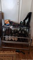 Front view of larger metal shoe rack holding boots, sandals, and shoes, showing three-tier rod design.