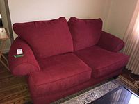 Front and side view showing red fabric loveseat with two seat cushions and two back cushions, rounded arms, and wooden base.