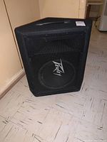 Front angled view of black Peavey speaker cabinet with metal grille and visible speaker cone inside.