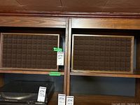 Pair of vintage speakers on wooden shelf with labeled tags showing no visible brand markings.