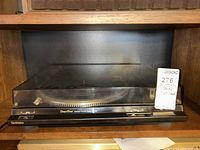 Front view of the Technics SL-DD22 turntable inside a wooden shelf with dust cover closed and a label card in the corner showing lot number and name.