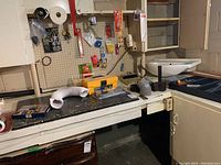 Workbench with assorted tools and hardware including hammer, sockets, plumbing parts, and decorative swans.