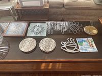 View of nine trivets on dark wood table showing variety of materials and designs