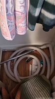 Coiled beige vacuum hose with metal wand and vacuum brush attachments on wooden floor.