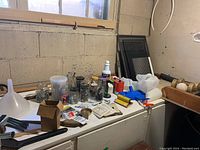 Photo of basement corner with jars, small tools, funnel, squeegee and hardware items on white chest freezer.