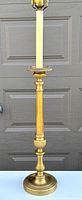 Front view of tall brass table lamp showing detailed base and column, white section below harp, and brass finial.