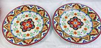 Two colorful El Centro Cuisinier ceramic dinner plates with floral and geometric patterns laid flat on a white surface, showing full top view of both plates.