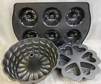 Metal baking pans featuring Nordic Ware bundt cake pans and Wilton shaped mold pan on white background
